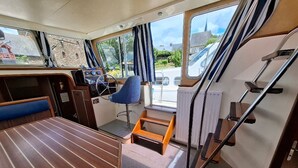 Ein gemütlicher Innenraum mit Bett, kleinem Tisch, Stuhl, Lenkrad und einem Fenster mit Vorhängen.