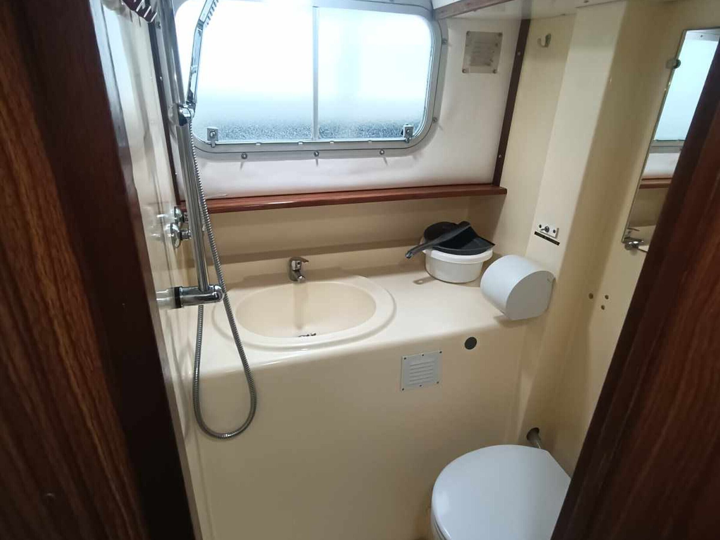 A compact bathroom with a window, a sink, a toilet, and a small storage area.