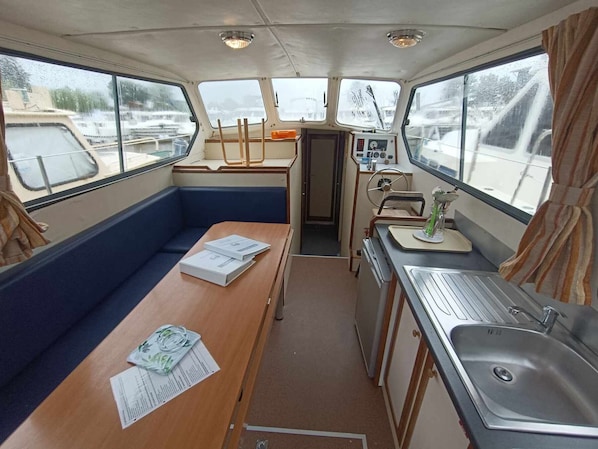 A compact galley with a bench, a small table with papers, a sink, and a control panel.