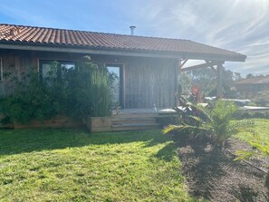 Ein Haus mit einem Ziegeldach, einer Holzdachterrasse und einem Garten mit verschiedenen Pflanzen.