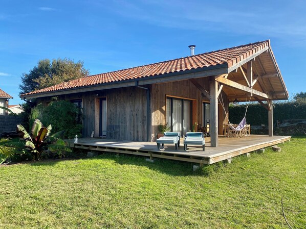 Ein Holzhaus mit Ziegeldach, einer Laube mit zwei Liegestühlen und einem kleinen Garten.