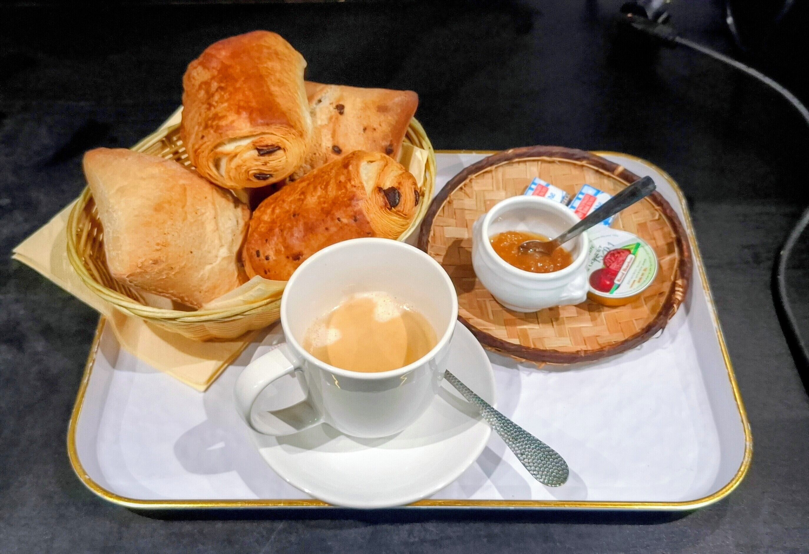 A tray with a cup of coffee, a small bowl of jam, and several pastries.