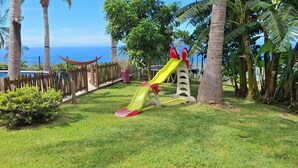 Un parque infantil con un tobogán y una hamaca, rodeado de palmeras y vistas al océano.