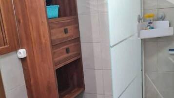 Une salle de bain avec un meuble-lavabo en bois, un lavabo blanc, un petit tabouret et un espace douche.