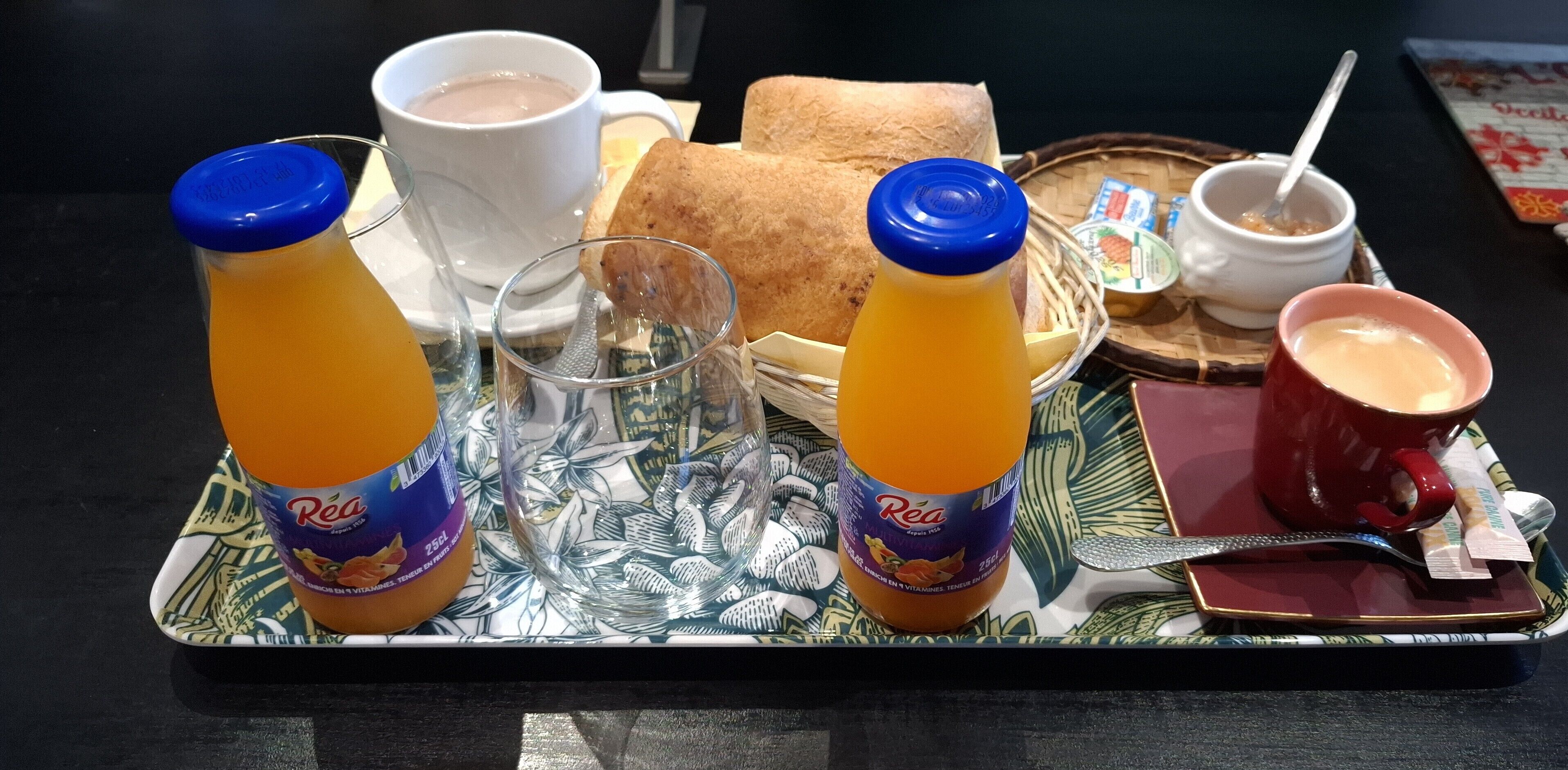 A tray with breakfast items including orange juice, a cup of coffee, a sandwich, and a bowl of yogurt.
