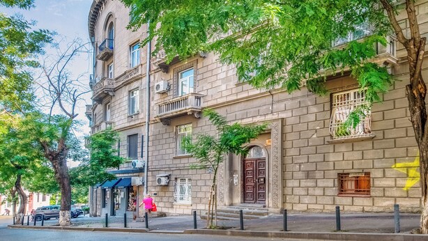 A multi-story building with a classic architectural style, featuring a central entrance with a large wooden door, multiple windows with decorative grilles, and a small balcony on the second floor. - HB apartments Astoria (Tbilisi)