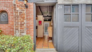 En smal indgang til en bygning med facade af mursten, flisegulv og en dør markeret med nummer 28.
