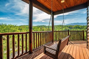 Un ponte di legno con una sedia a dondolo, una ringhiera in legno e vista su un paesaggio boschivo.
