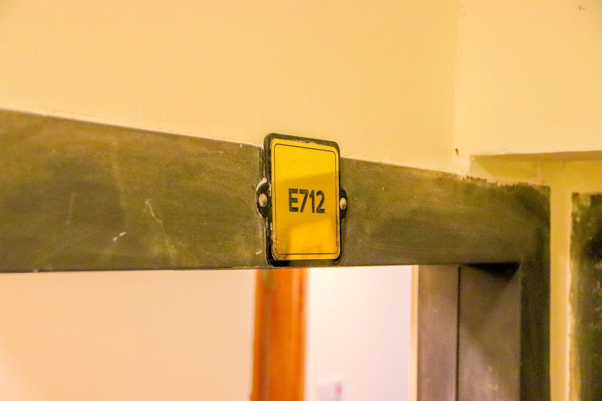 Una señal amarilla con el número 'E712' adherido a una estructura metálica.