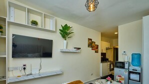A compact living space with a bed, a TV mounted on the wall, a small kitchen area, and a dining table. - Studio Sleeps 2 With 24hr Check-in (Syokimau)