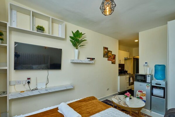 Espaço compacto com cama, televisão na parede, pequena cozinha e mesa de jantar.