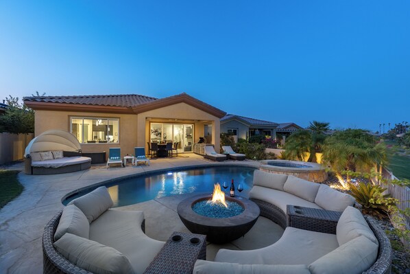 A swimming pool with a fire pit, outdoor seating, and a covered patio area.