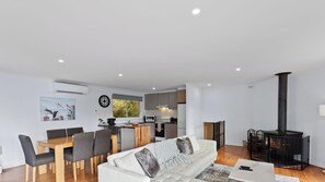 A modern living room with a sofa, dining table, and chairs, a kitchen area with a stove, and a fireplace.