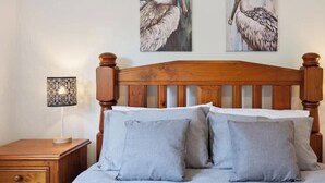 A bedroom with a wooden headboard, a bedside table with a lamp, and two wall-mounted paintings of pelicans.