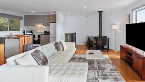 A modern living room with a sofa, a flat-screen TV, a fireplace, and a kitchen area with cabinets and appliances.