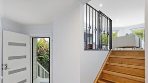 A modern interior with a wooden staircase, a white door, and a view through a glass door to a balcony with greenery.
