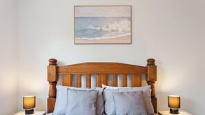 A bedroom with a wooden headboard, two bedside lamps, and a framed painting of a beach scene.