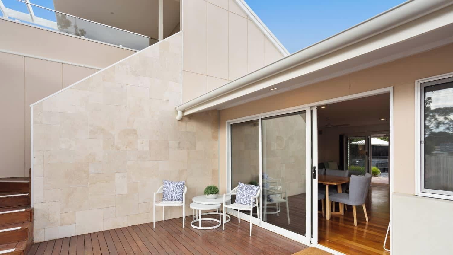 A modern house with a wooden deck, a glass door leading to a dining area, and a staircase.