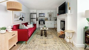 A modern kitchen with white cabinets, a built-in oven, and a TV mounted above the fireplace.