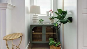 A hallway with a green cabinet, a lamp, a small round table, and potted plants.