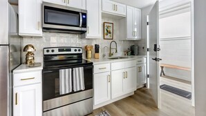 A compact kitchen with white cabinets, a stainless steel stove, a microwave, and a sink.