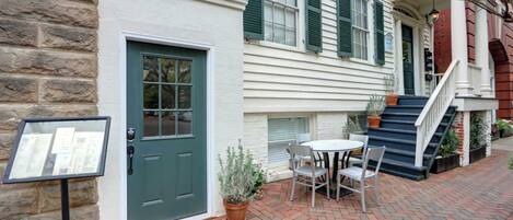 A two-story building with a green door, a brick staircase, and a small outdoor seating area with a table and chairs.