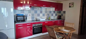 Una cocina con armarios rojos, un microondas, un horno y una mesa de comedor con sillas.