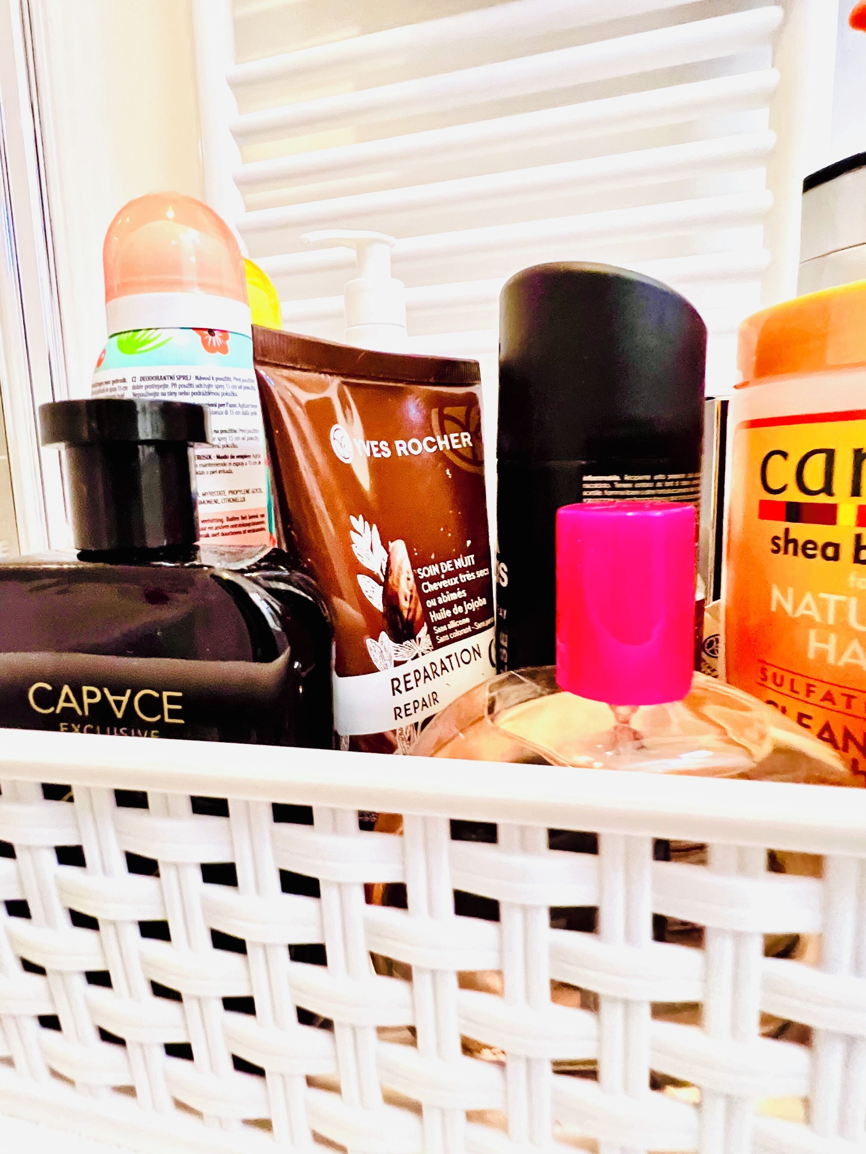 A basket containing various toiletries including a bottle of Caprice, a tube of Reparation, and a bottle of shampoo.