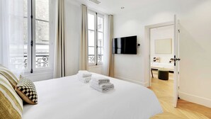 Ett hotellrum med en säng, en tv som är monterad på väggen och ett badrum som syns genom en öppen dörr.