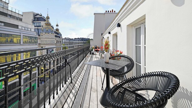 En balkong med ett bord och stolar, ett räcke och utsikt över stadsbilden.