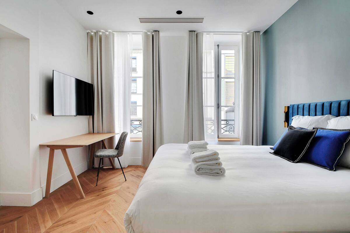 A hotel room with a bed, a desk, a chair, a TV, and a balcony view.