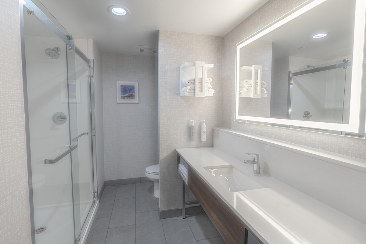 A modern bathroom with a glass shower enclosure, a white sink, and a large mirror.