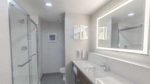 Un baño moderno con cabina de ducha de vidrio, un lavabo blanco y un espejo grande.