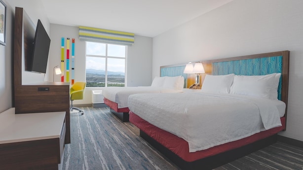 Habitación de hotel con dos camas, un escritorio, televisor, ventana con vistas y una lámpara.