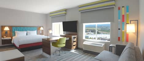 Habitación de hotel con cama, escritorio, silla, televisión y un amplio ventanal con vistas a la ciudad.