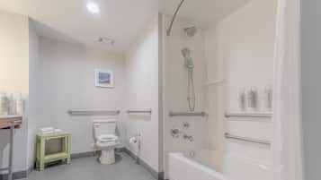 Un baño moderno con inodoro, ducha y bañera. Hay barras de apoyo y un pequeño estante con artículos de aseo.