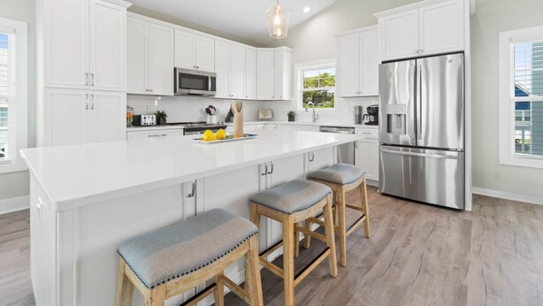 A modern kitchen with white cabinetry, a stainless steel refrigerator, and a large island with stools.