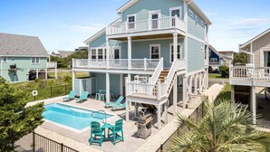 A two-story house with a balcony, a swimming pool, and outdoor furniture.