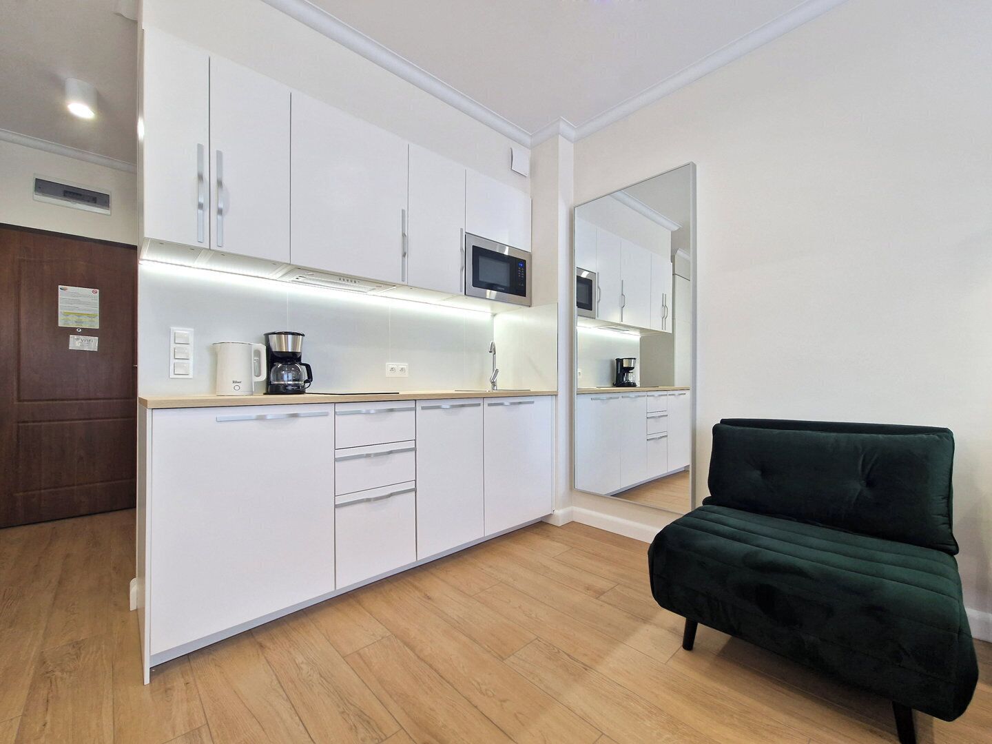 A modern kitchen with white cabinets, a microwave, and a coffee maker. There is a green chair in the room.
