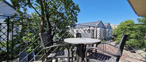 An outdoor patio with a round table and two chairs, surrounded by a metal fence.