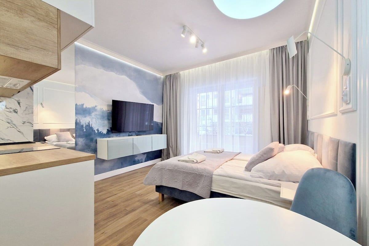 Une chambre d’hôtel moderne équipée d’un lit, d’un bureau, d’une télévision à écran plat et d’une grande fenêtre avec des rideaux.