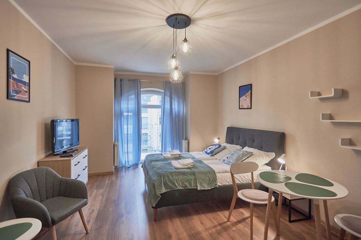 Une chambre à coucher avec un lit, un bureau, une chaise, une télévision et une fenêtre avec des rideaux.