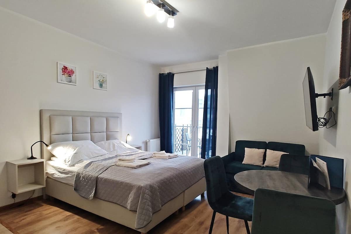Une chambre à coucher comprenant un lit, des tables de chevet, un bureau, des chaises, une fenêtre avec des rideaux et des œuvres d’art accrochées au mur.