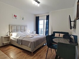 A bedroom with a bed, bedside tables, a desk, chairs, a window with curtains, and wall-mounted artwork.