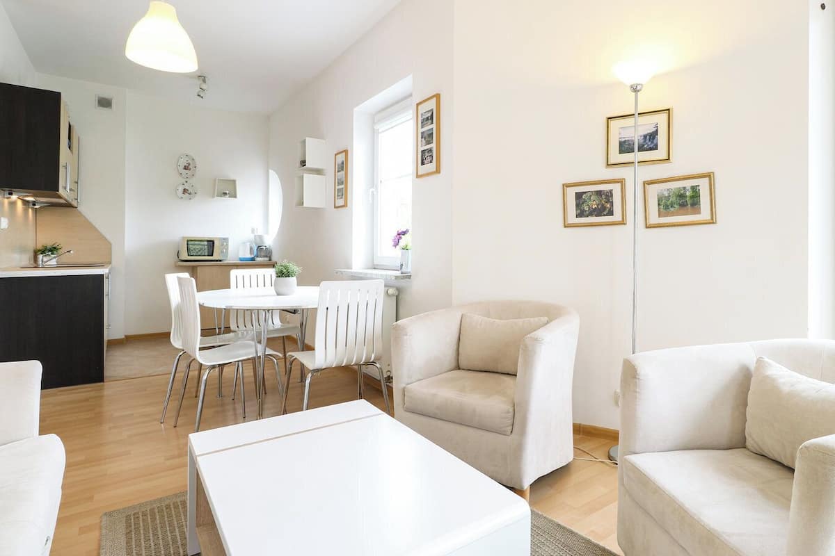 Un salon moderne et bien éclairé, avec un canapé blanc, une table basse blanche et un coin repas comprenant une table et des chaises blanches.