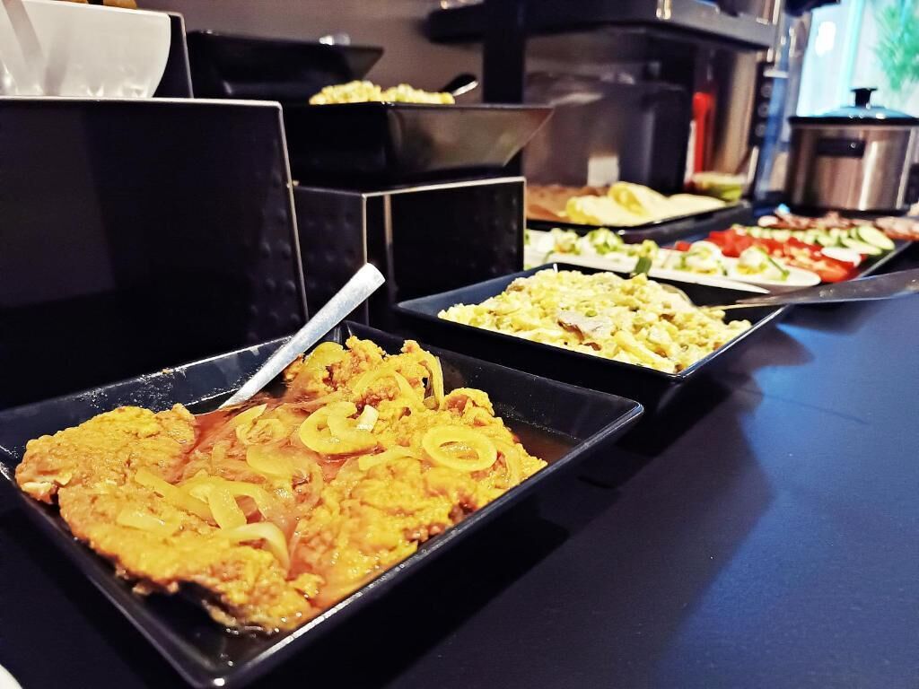Een buffet met diverse gerechten, waaronder een gele curry, een groentengerecht en een salade.