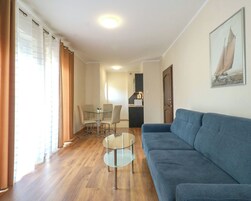 A modern living room with a blue sofa, a glass coffee table, and a dining area with chairs and a table.