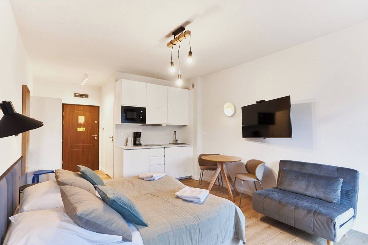 Une chambre d’hôtel moderne équipée d’un lit, d’un canapé, d’une table à manger avec des chaises, d’un coin cuisine et d’un téléviseur fixé au mur.