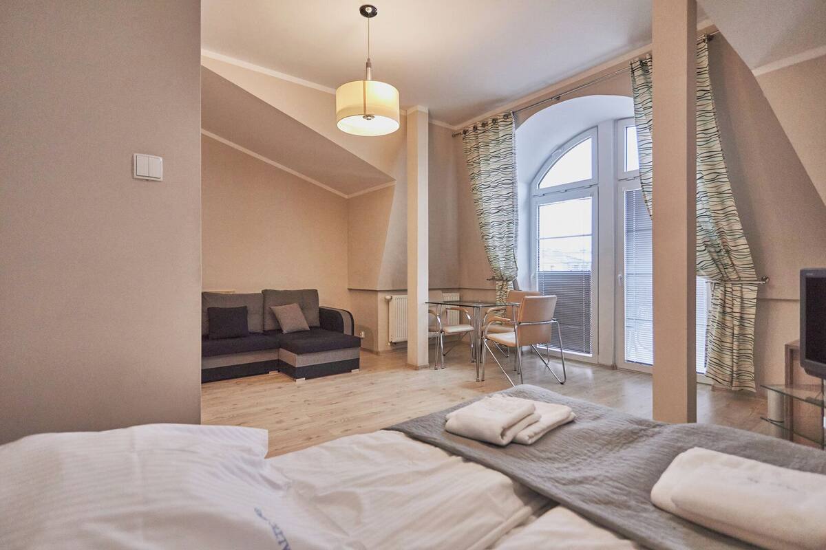 Une chambre d’hôtel moderne équipée d’un lit, d’un canapé, d’une table à manger avec des chaises, d’une télévision et d’une grande fenêtre avec des rideaux.