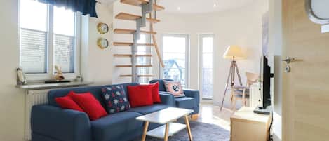 Una sala de estar moderna con un sofá azul, una escalera de madera, una mesita y una lámpara.